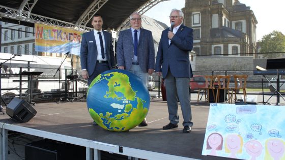 Drei Männer stehen auf der Bühne vor einem Globus.