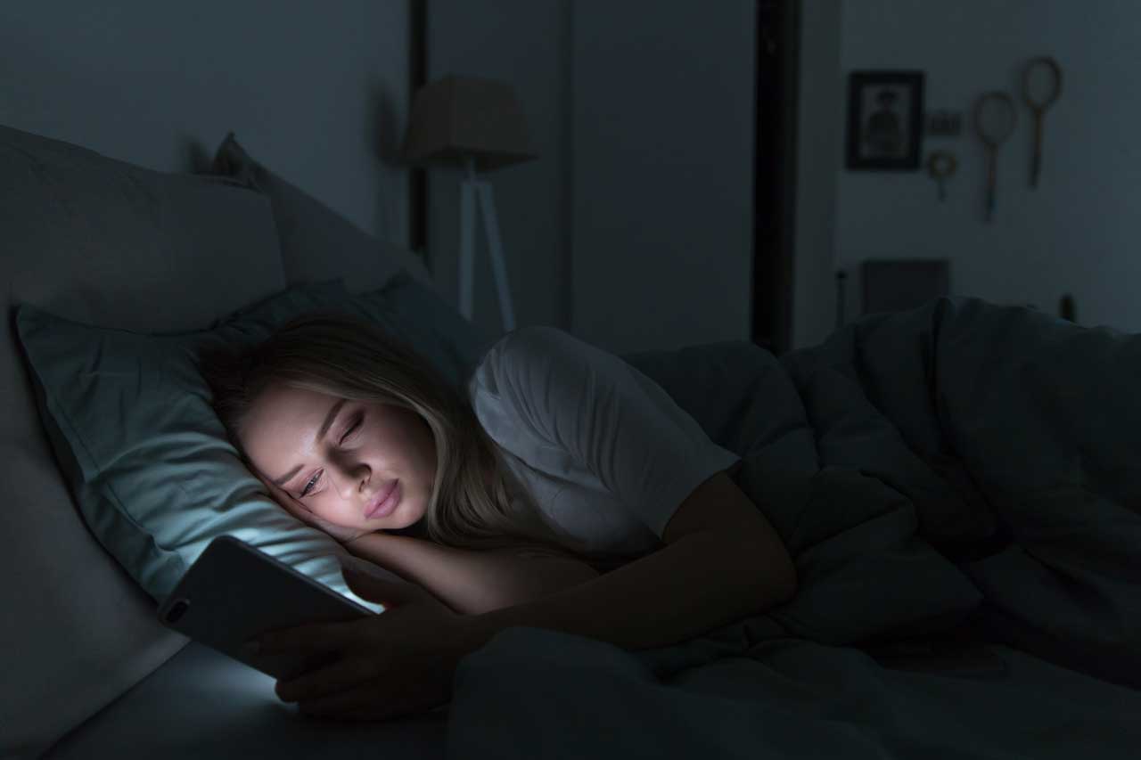 Junge Frau liegt mit Smartphone im Bett.