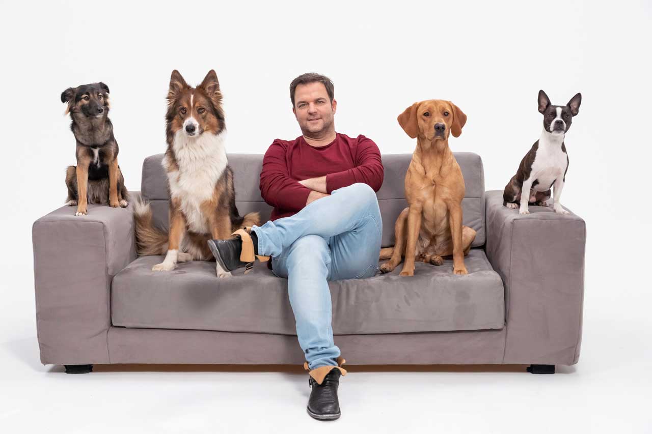 Mann sitzt mit vier Hunden auf der Couch.