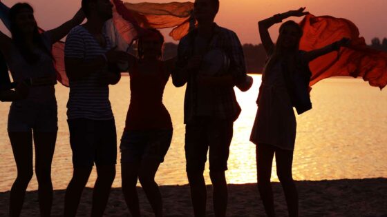 Jugendliche tanzen am Strand bei Sonnenuntergang