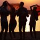 Jugendliche tanzen am Strand bei Sonnenuntergang